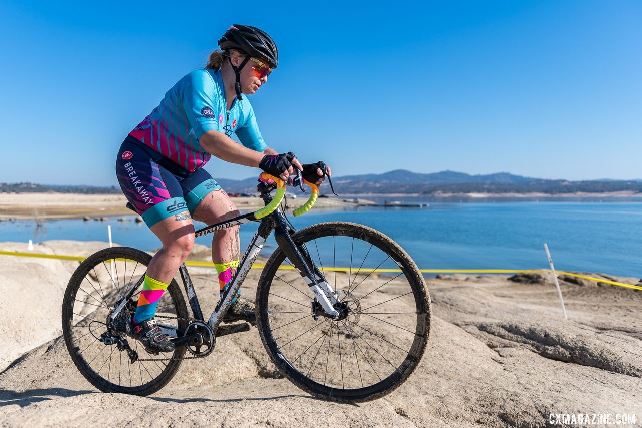 First-year 'crosser Autumn Hardy prepares to descend the large rock feature with Folsom Lake as a backdrop. 2019 Sacramento CX Granite Beach, California. © Jeff Vander Stucken