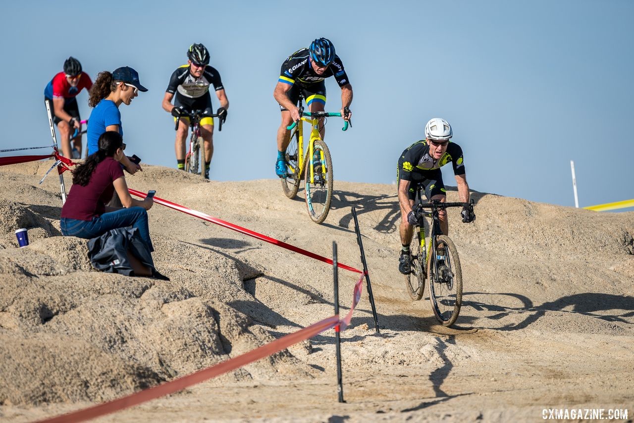 Masters B racers descend off of the rock. There were multiple lines up the far side that converged on a single route down to the lake edge. 2019 Sacramento CX Granite Beach, California. © Jeff Vander Stucken